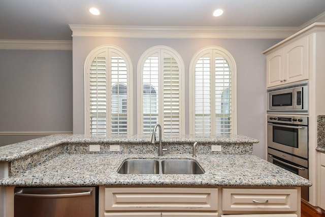 kitchen with a sink, appliances with stainless steel finishes, ornamental molding, and light stone counters