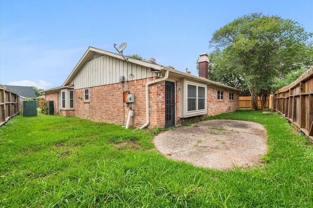 rear view of property featuring a yard, brick siding, a chimney, and a fenced backyard