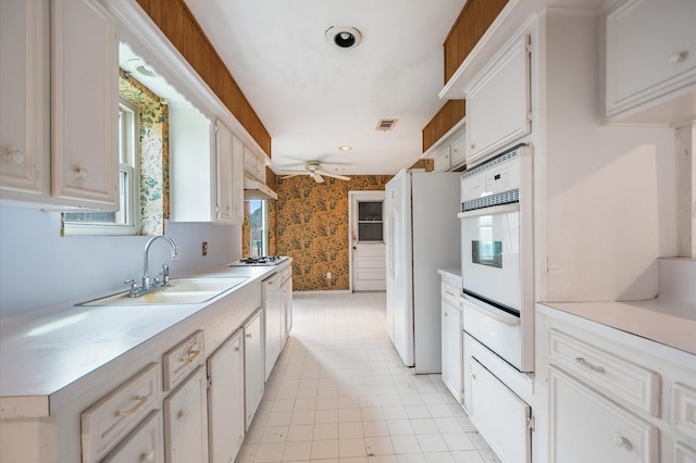 kitchen with a sink, white appliances, light countertops, wallpapered walls, and a warming drawer