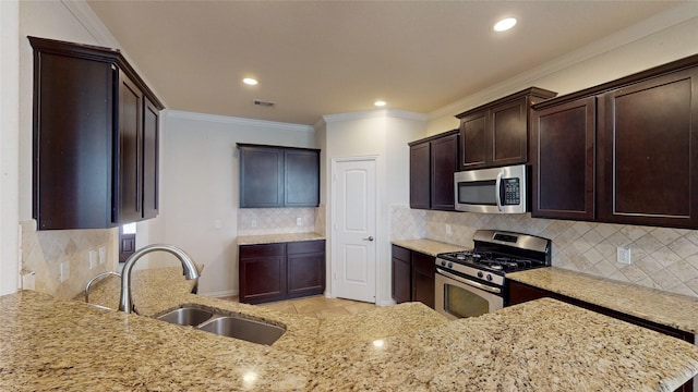 kitchen featuring light stone countertops, dark brown cabinetry, a sink, stainless steel appliances, and backsplash