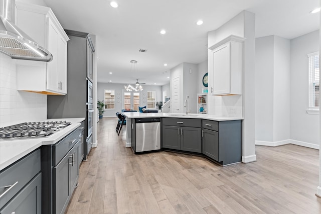kitchen featuring wall chimney range hood, gray cabinets, stainless steel appliances, and a sink
