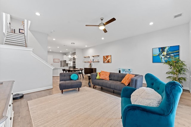living room featuring stairs, visible vents, ceiling fan with notable chandelier, and light wood-style floors