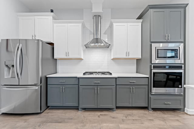 kitchen featuring gray cabinetry, wall chimney range hood, stainless steel appliances, and tasteful backsplash