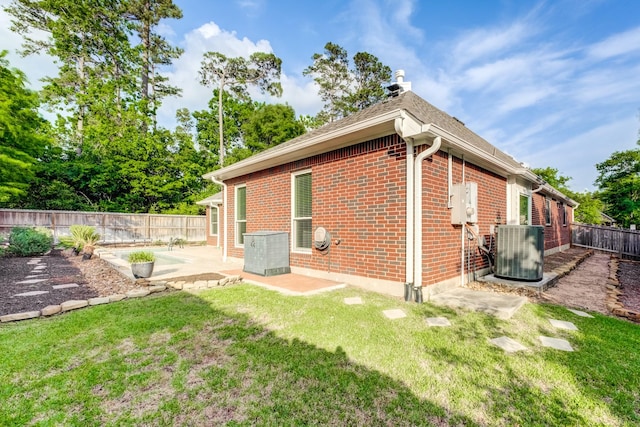 view of side of property featuring brick siding, a patio, central AC, and a yard