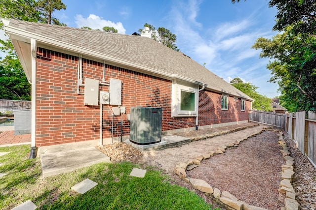 back of house featuring roof with shingles, brick siding, a fenced backyard, a chimney, and central air condition unit