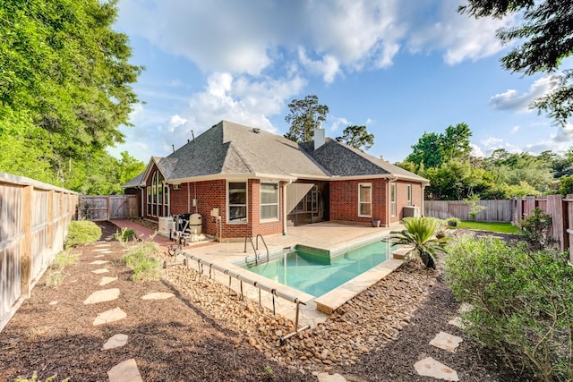 rear view of house with a fenced backyard, a chimney, brick siding, a fenced in pool, and a patio area