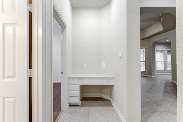 hallway with arched walkways, baseboards, and light tile patterned floors
