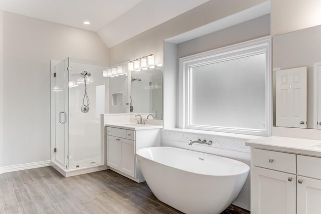 full bathroom featuring a freestanding bath, two vanities, wood finished floors, and a stall shower