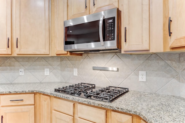 kitchen featuring light brown cabinetry, light stone counters, black gas stovetop, stainless steel microwave, and decorative backsplash