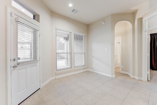 interior space with arched walkways, baseboards, visible vents, and light tile patterned floors