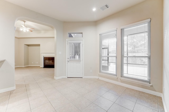 empty room with visible vents, a ceiling fan, baseboards, a fireplace with flush hearth, and light tile patterned floors