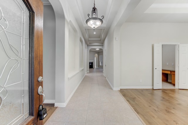 hallway featuring arched walkways, baseboards, light tile patterned flooring, and a raised ceiling