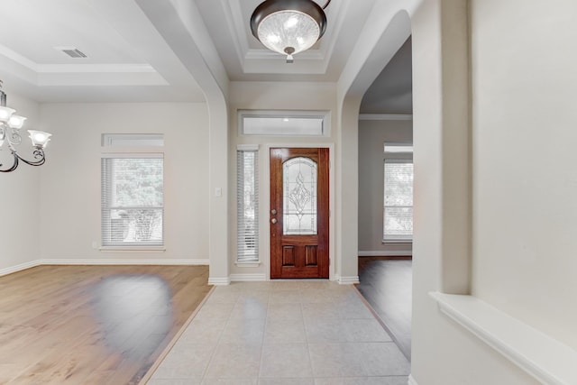 entryway with a notable chandelier, arched walkways, a tray ceiling, visible vents, and ornamental molding