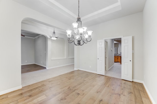 unfurnished dining area featuring light wood-style floors, arched walkways, crown molding, and an inviting chandelier