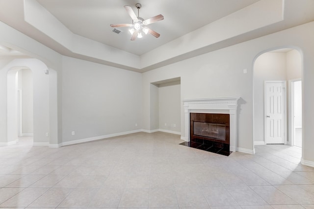 unfurnished living room featuring light tile patterned floors, arched walkways, ceiling fan, and a tray ceiling