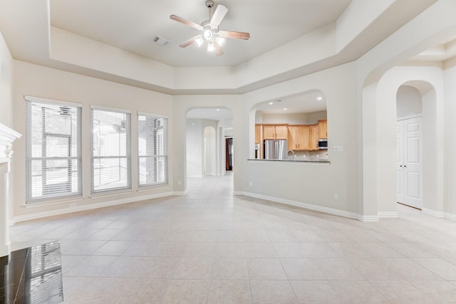 unfurnished living room featuring light tile patterned flooring, ceiling fan, arched walkways, baseboards, and visible vents
