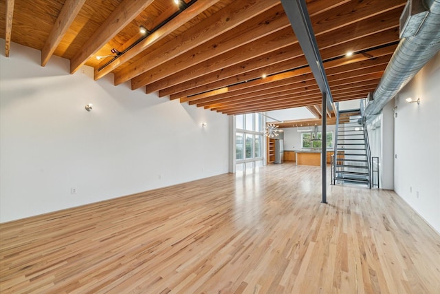 unfurnished living room with stairway, beamed ceiling, and light wood-style flooring