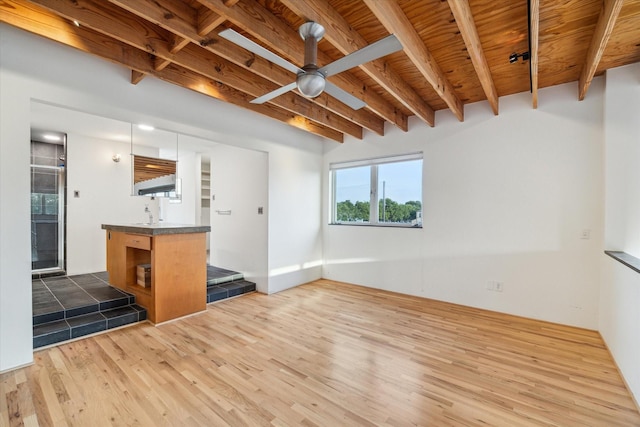 unfurnished living room with beam ceiling, a ceiling fan, and wood finished floors