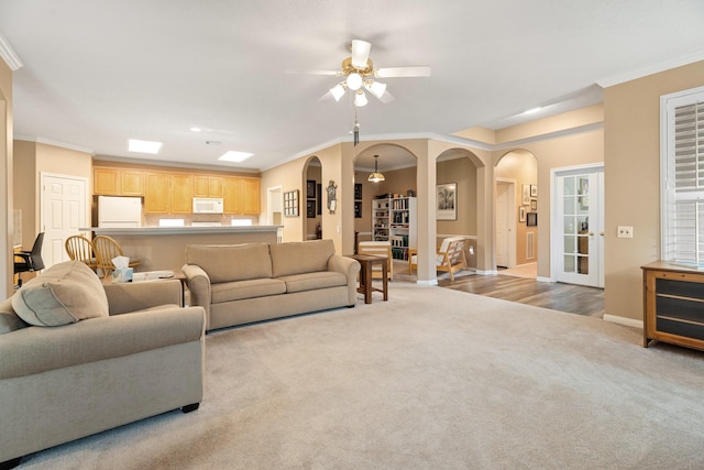 living room featuring a ceiling fan, crown molding, arched walkways, baseboards, and carpet floors
