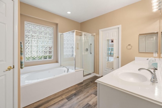 full bath with a garden tub, double vanity, wood finished floors, a sink, and a stall shower
