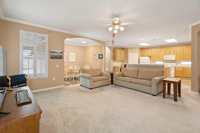 living room with crown molding, baseboards, ceiling fan, light colored carpet, and arched walkways