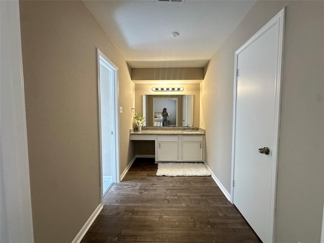 hallway featuring dark wood-type flooring, a sink, and baseboards