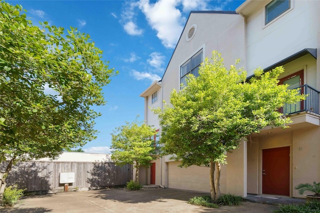 view of property exterior featuring concrete driveway, stucco siding, fence, and an attached garage