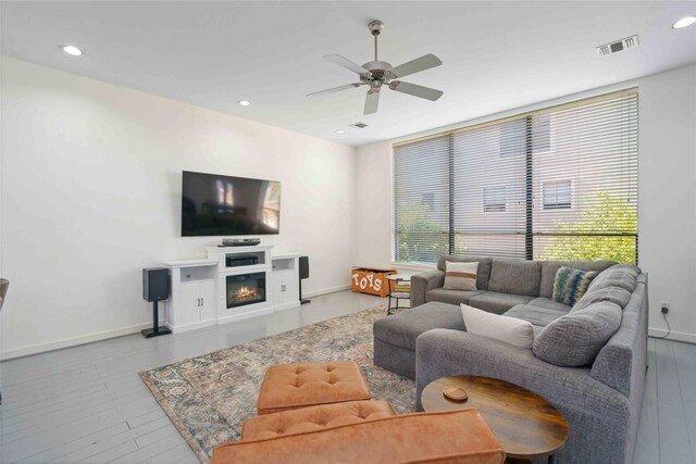 living area featuring a ceiling fan, wood finished floors, baseboards, recessed lighting, and a glass covered fireplace