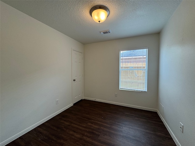 empty room with a textured ceiling, baseboards, visible vents, and dark wood-style floors