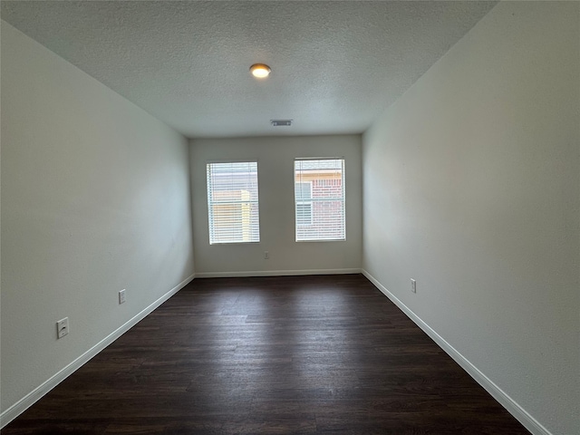 empty room featuring baseboards, dark wood-type flooring, a textured ceiling, and visible vents