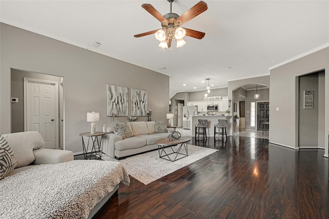 living area featuring arched walkways, dark wood finished floors, ceiling fan, and ornamental molding