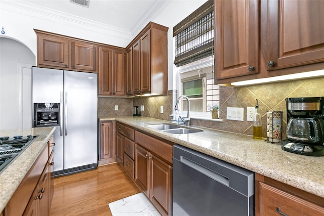 kitchen featuring crown molding, appliances with stainless steel finishes, a sink, light stone counters, and light wood-style flooring