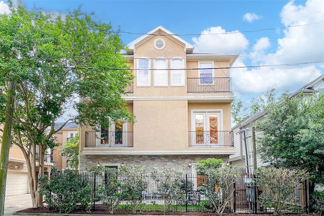 exterior space featuring stone siding, a fenced front yard, stucco siding, and a balcony
