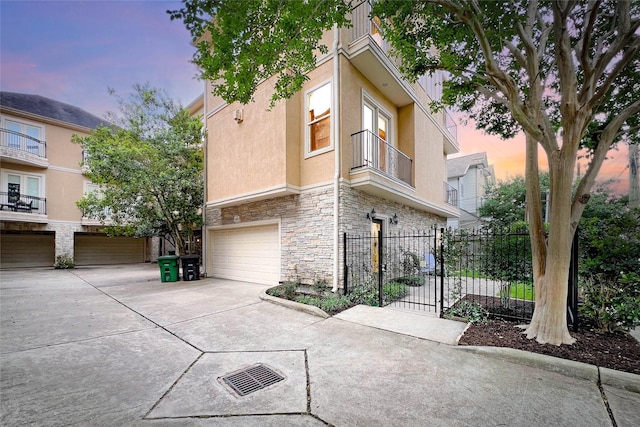 view of home's exterior with a garage, fence, concrete driveway, stone siding, and stucco siding