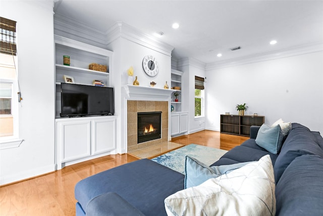 living room with visible vents, crown molding, built in features, baseboards, and light wood-style floors