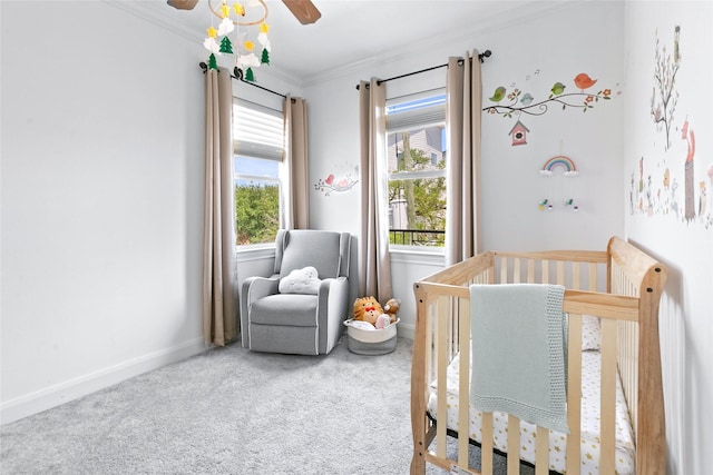 carpeted bedroom with crown molding, a ceiling fan, a crib, and baseboards