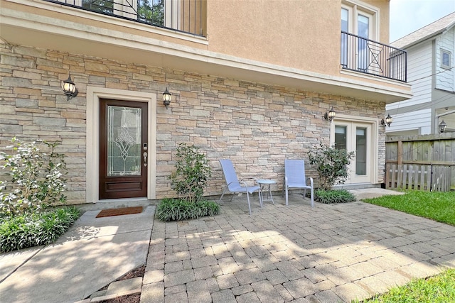 doorway to property with fence, a balcony, a patio, stone siding, and stucco siding
