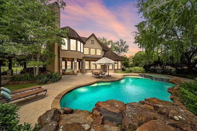 pool at dusk featuring a patio, fence, and a pool with connected hot tub