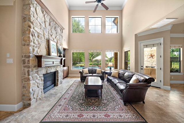 living area featuring baseboards, a fireplace, crown molding, ceiling fan, and healthy amount of natural light