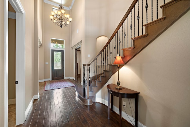 foyer featuring dark wood-type flooring, baseboards, a chandelier, a high ceiling, and stairs