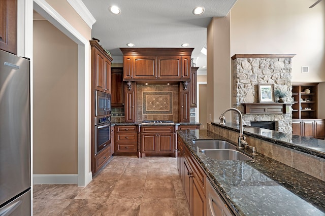 kitchen featuring a sink, stainless steel appliances, dark stone countertops, a fireplace, and recessed lighting