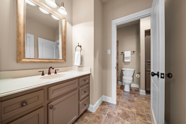 bathroom with stone tile floors, baseboards, toilet, and vanity