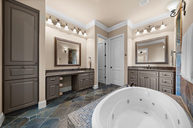full bath with ornamental molding, a tub with jets, baseboards, two vanities, and stone finish floors