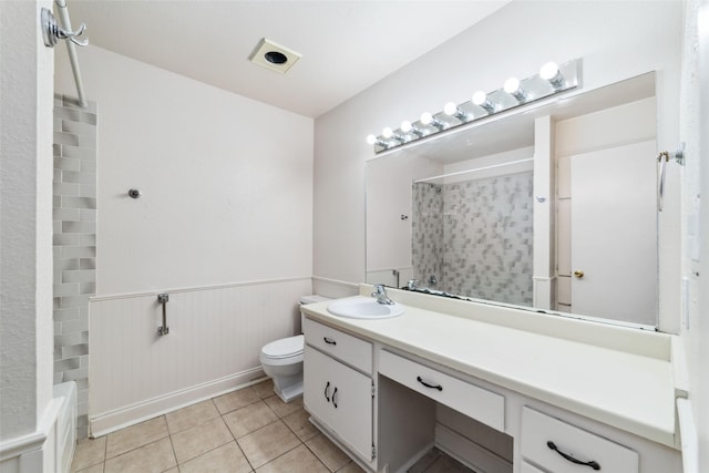 full bath featuring tile patterned flooring, vanity, toilet, a wainscoted wall, and a shower