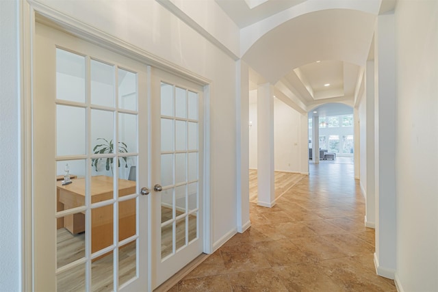 corridor featuring arched walkways, baseboards, and french doors