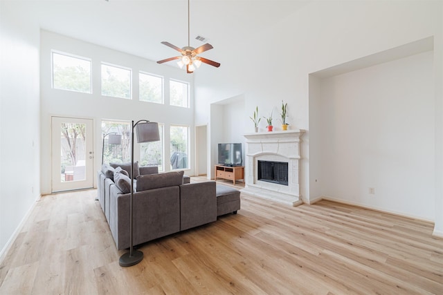 living area with a healthy amount of sunlight, ceiling fan, a fireplace with raised hearth, and light wood-style flooring
