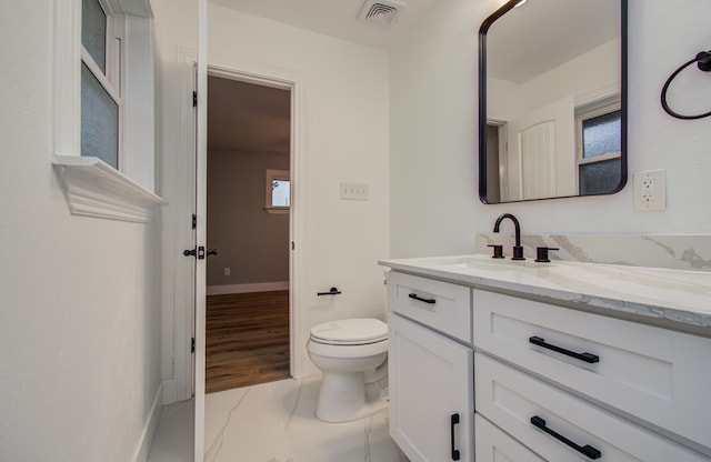 half bath featuring visible vents, baseboards, toilet, and vanity