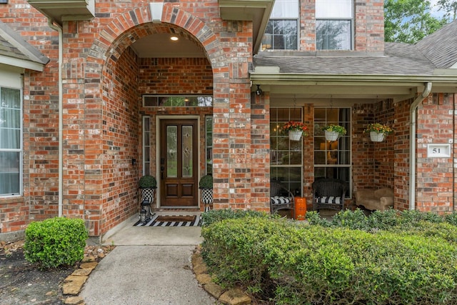 doorway to property with roof with shingles and brick siding