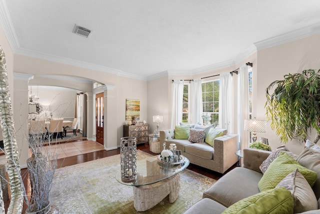 living room with decorative columns, visible vents, arched walkways, wood finished floors, and ornamental molding