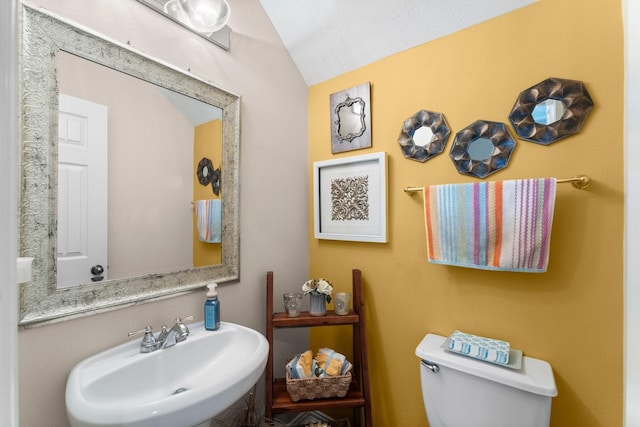 half bath with toilet, vaulted ceiling, and a sink